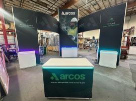 RENTAL: RE-9170 Island Design with 80" Wide x 42" Deep x 190" High Gravitee Storage Tower, (2) Gravitee Double-Sided Curved Bridged Headers, (2) Double-Sided Front Kiosks, (4) Large Monitor Mounts, RE-1577 White Laminated Reception Counter, RE-1576 White